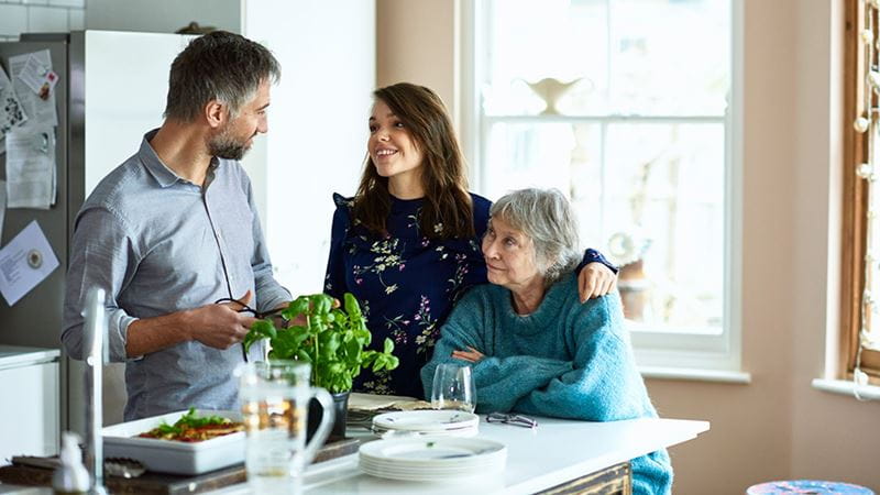 Parent, child and elderly person preparing dinner and talking about retirement plans.
